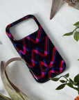 Phone case with colorful zigzag pattern on a white surface with green leaves