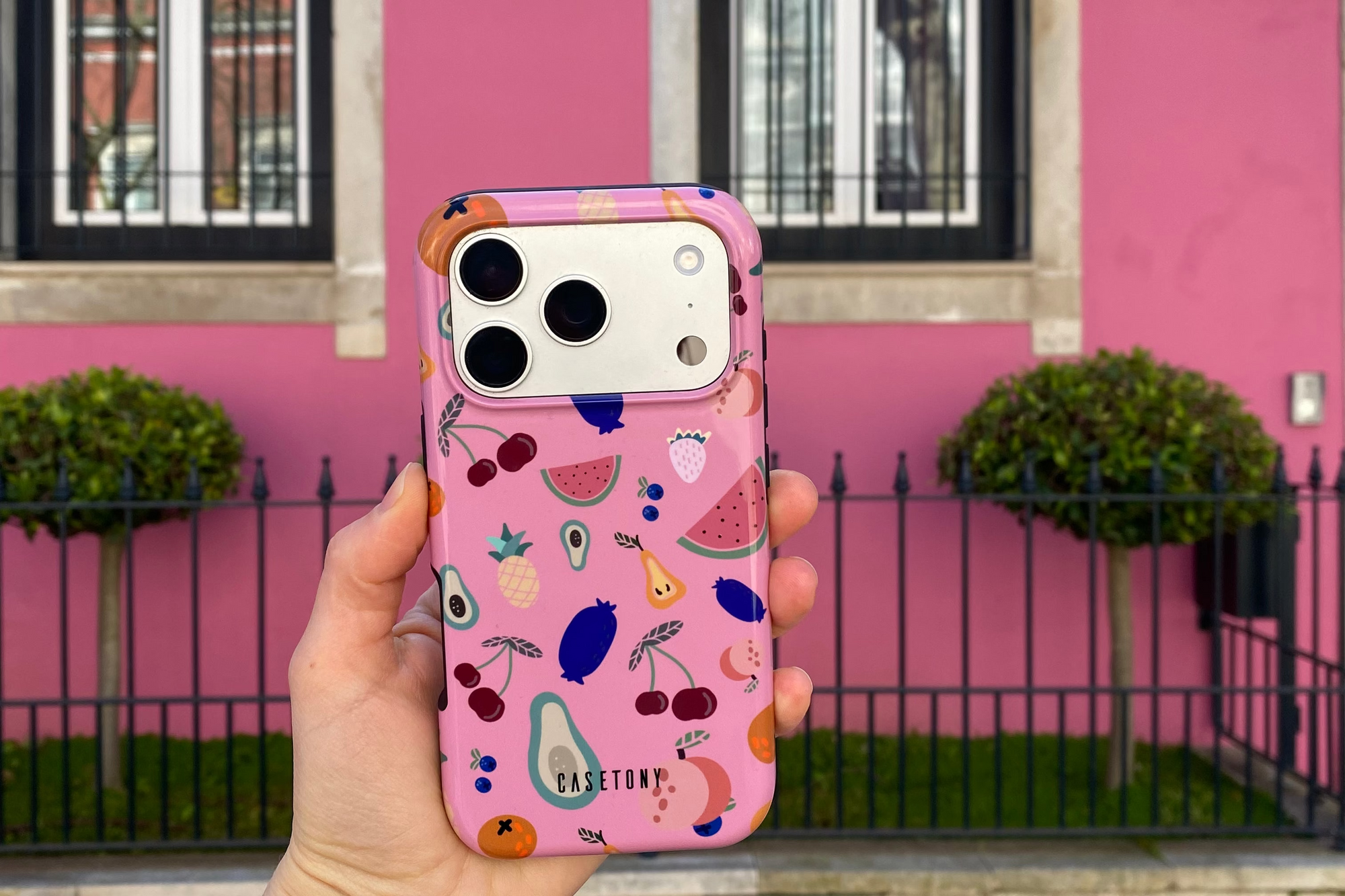 Hand holding a phone with a colorful case in front of a pink building