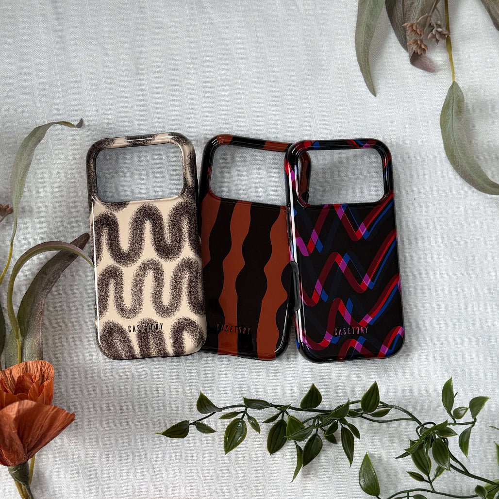 Three patterned phone cases on a white surface with floral and leaf decorations.