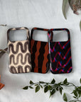 Three patterned phone cases on a white surface with floral and leaf decorations.