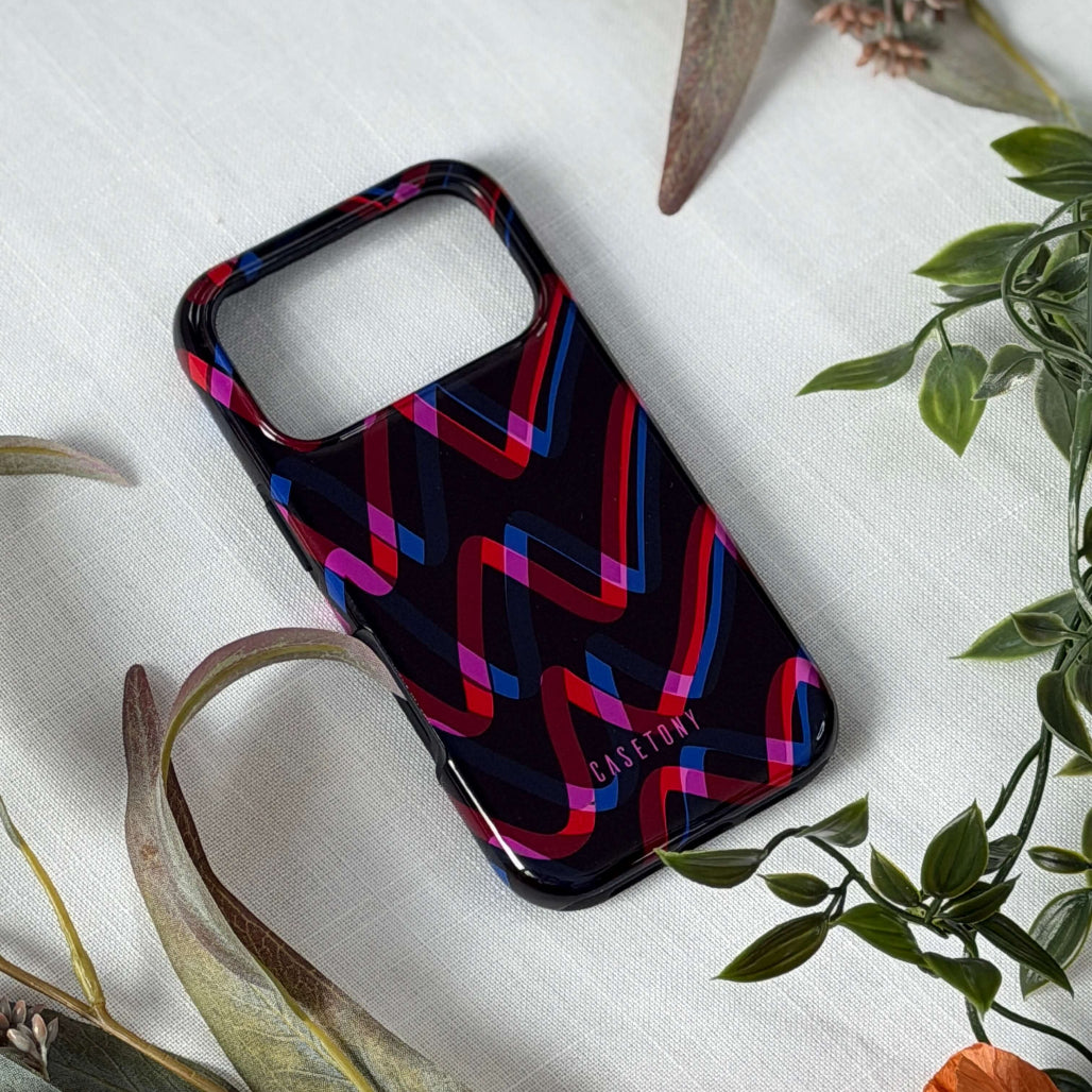 Phone case with colorful zigzag pattern on a white surface with green leaves